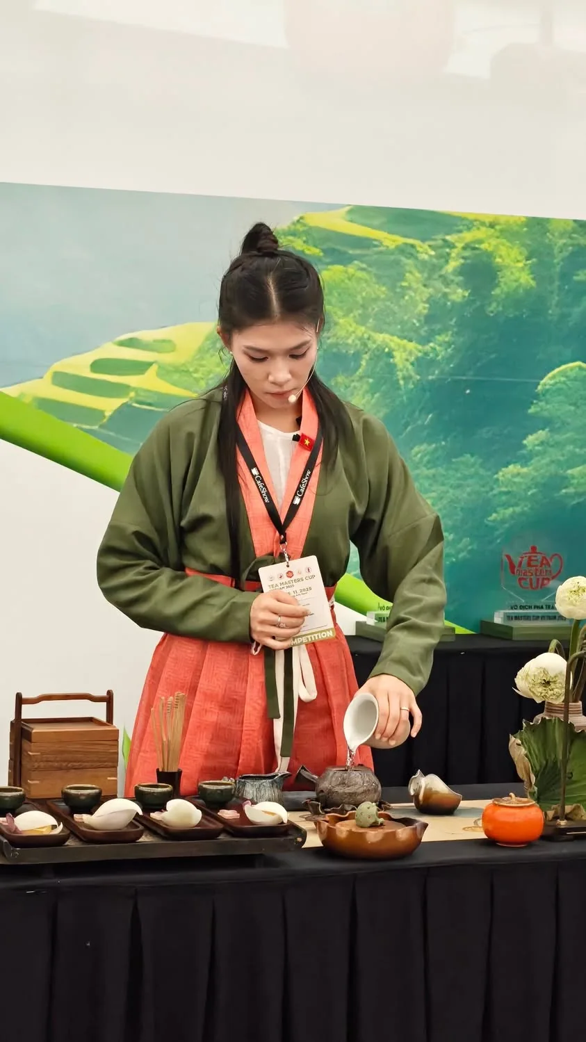Vy Đan trong áo xanh rêu và váy đỏ cam tại bàn thi Tea Masters Cup