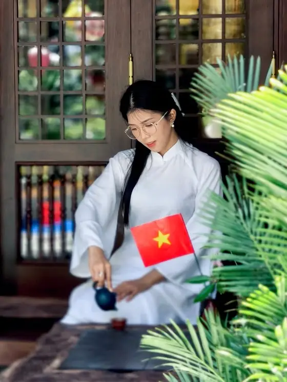Áo dài trắng bên bàn trà và lá cờ nhỏ