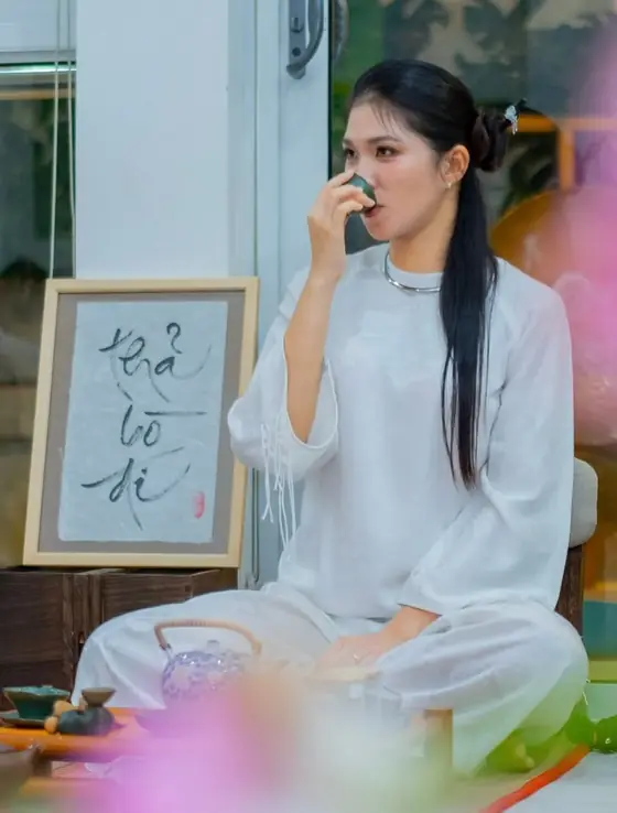 Vy Đan áo trắng bên bức thư pháp